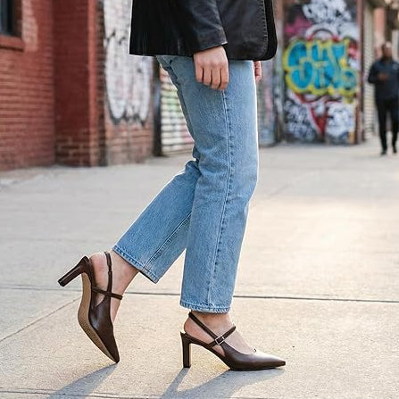 Person wearing blue jeans and brown high-heeled shoes on a city street with graffiti in the background.